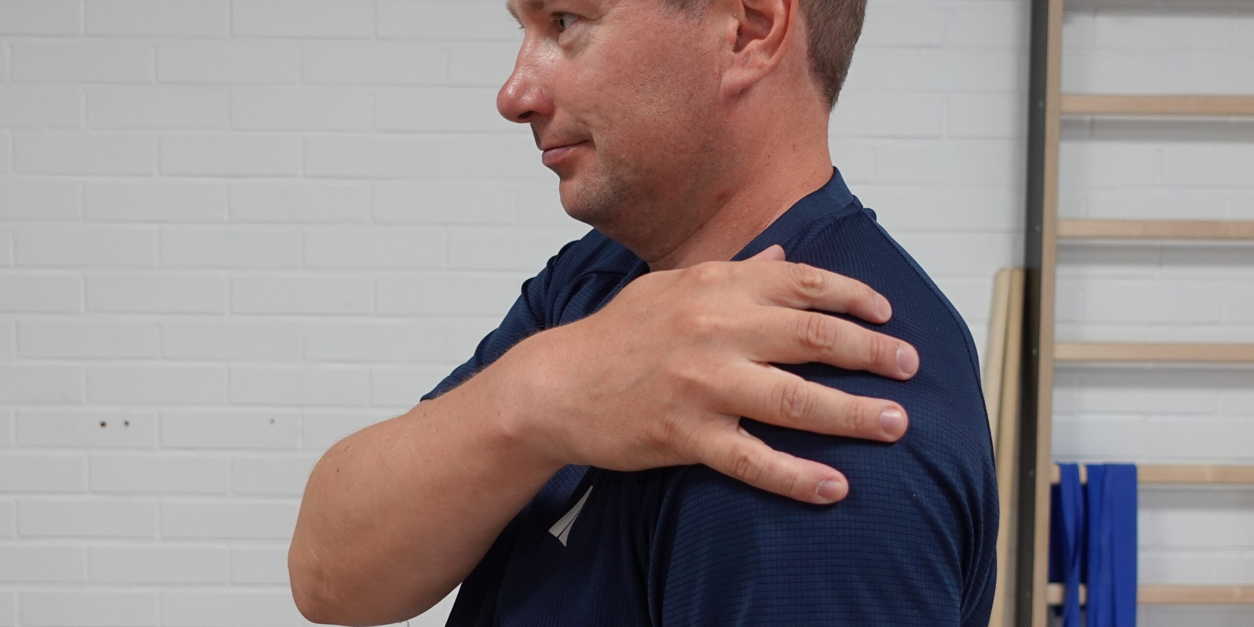 Fysioterapeutti näyttää olkapään kipukohtaa sivulta katsottuna pitelemällä omaa olkapäätään.