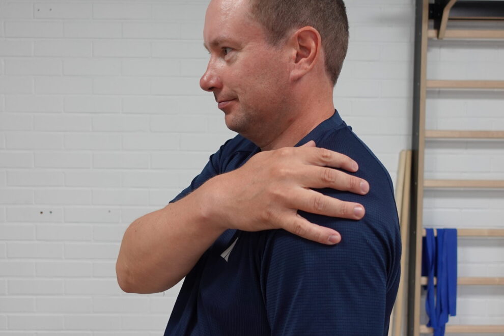 Fysioterapeutti näyttää olkapään kipukohtaa sivulta katsottuna pitelemällä omaa olkapäätään.