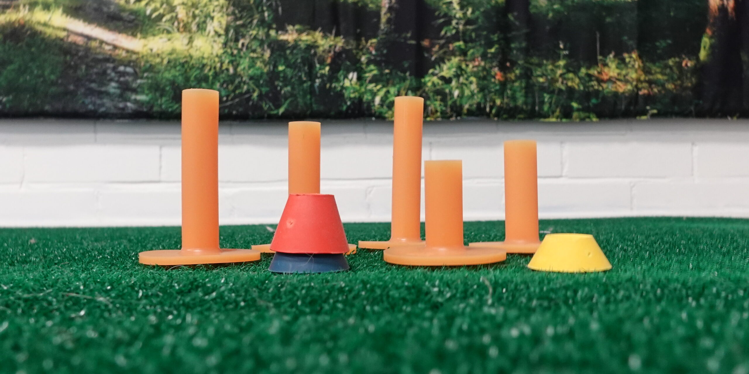 Lattiatasosta otettu kuva lyöntimaton reunalle asetetuista erimittaisista kumisista tiistä, jotka korostavat kehon mittasuhteiden merkitystä golfissa.