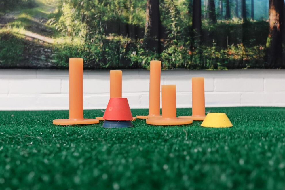 Lattiatasosta otettu kuva lyöntimaton reunalle asetetuista erimittaisista kumisista tiistä, jotka korostavat kehon mittasuhteiden merkitystä golfissa.