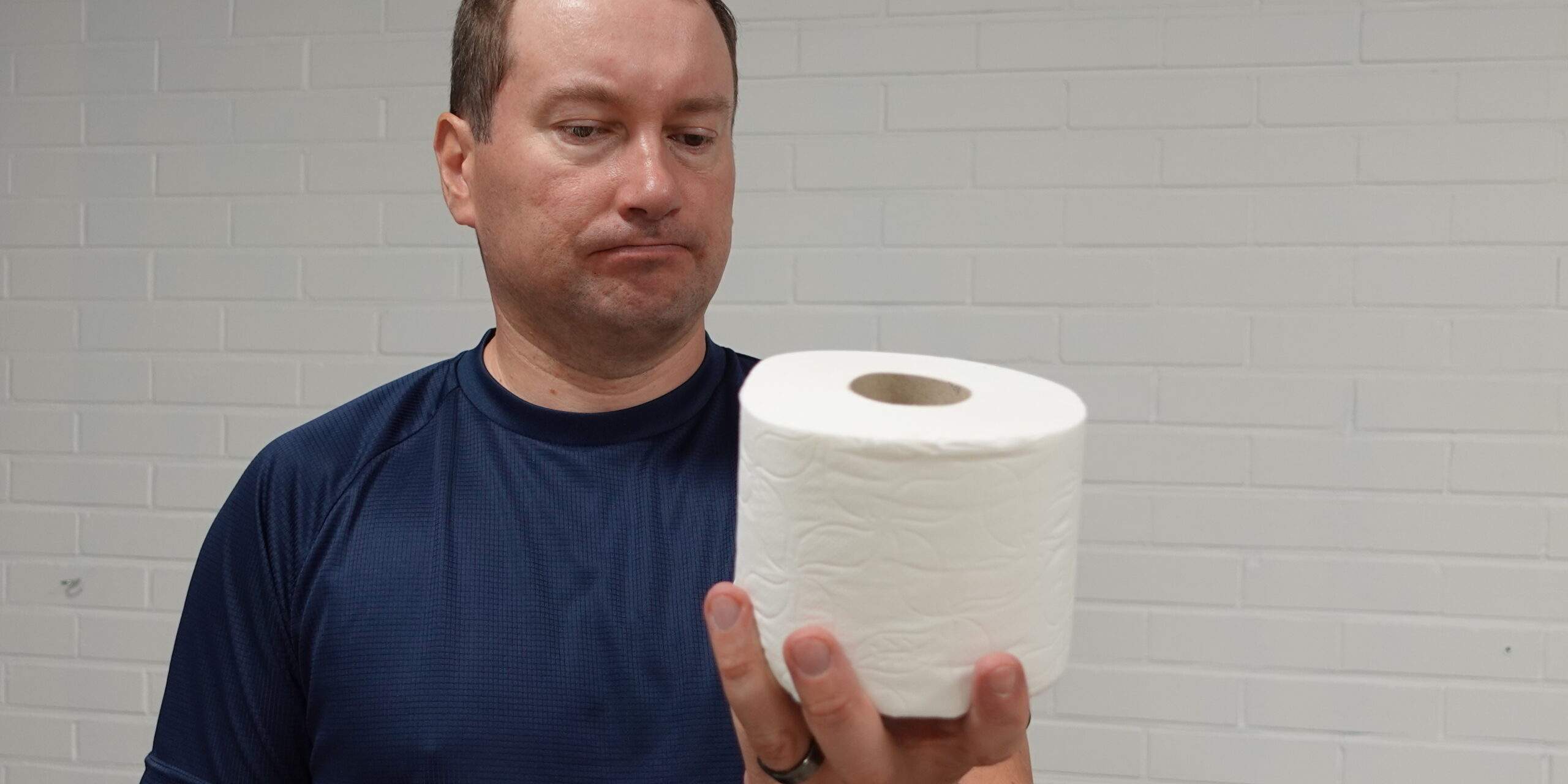 Henkilö pitelee wc-paperirullaa rinnan korkeudella ja katsoo sitä mietteliäänä – kuva havainnollistaa jäätyneen olkapään vaikutusta arjen liikkeisiin.