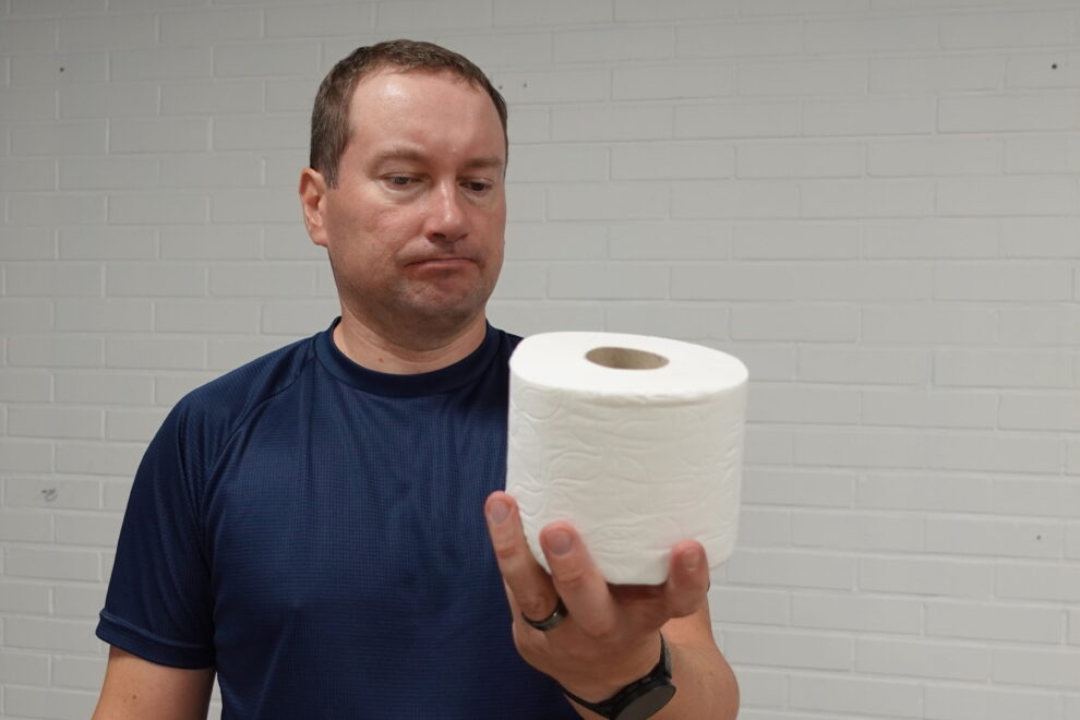 Henkilö pitelee wc-paperirullaa rinnan korkeudella ja katsoo sitä mietteliäänä – kuva havainnollistaa jäätyneen olkapään vaikutusta arjen liikkeisiin.