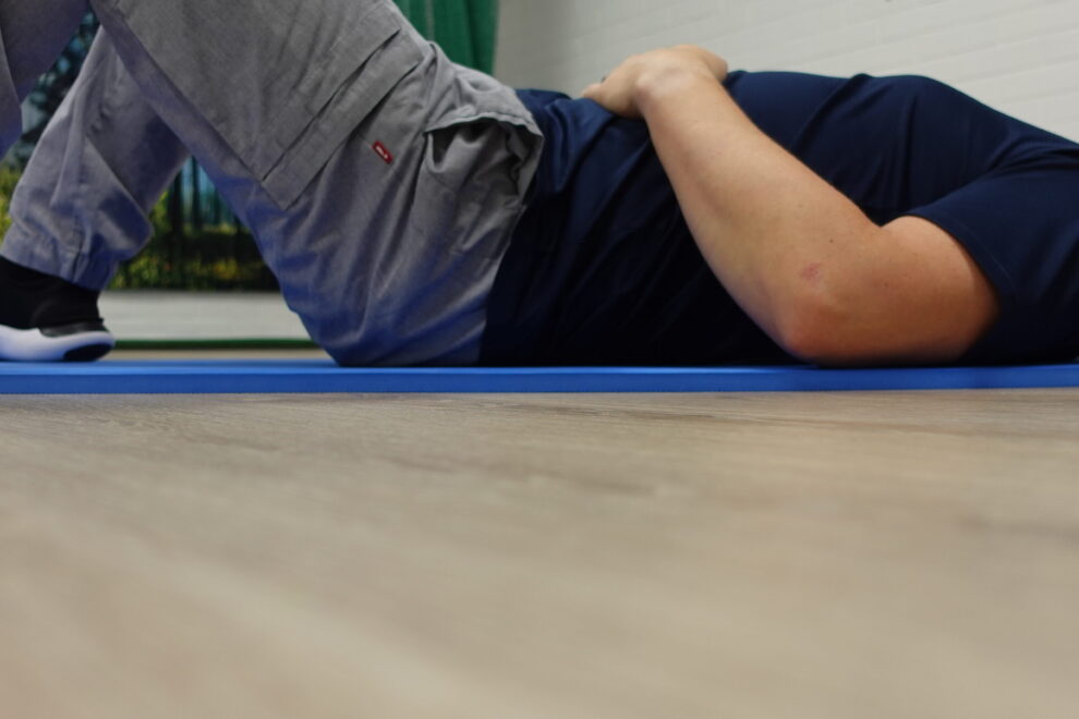 Selinmakuulla oleva mies tekee lantionpohjan jännitysharjoitetta, käsi vatsan päällä. Harjoitus tukee hermoston rauhoittumista ja kehon tasapainoa fysioterapiassa Joensuussa.