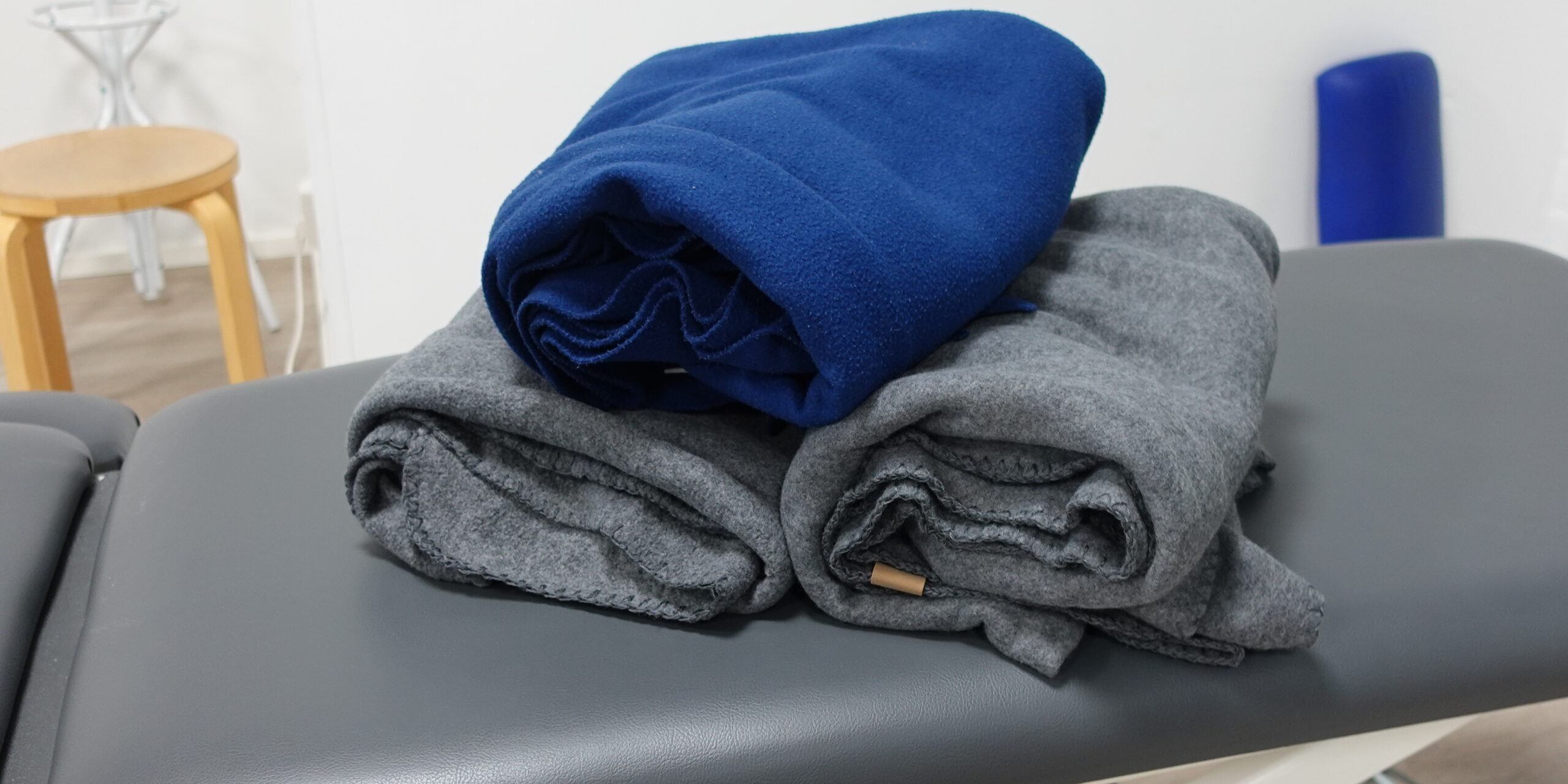 Rullalle käärittyjä fleesepeittoja hoitopöydän päällä. Kuva liittyy hierontaan ja kehon hyvinvointiin Joensuussa.