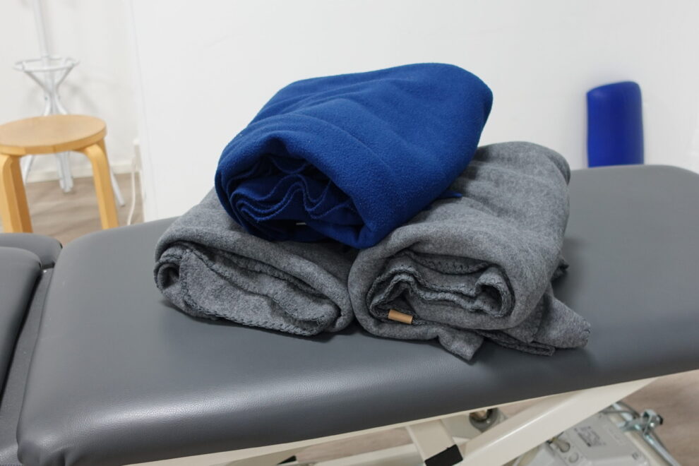 Rullalle käärittyjä fleesepeittoja hoitopöydän päällä. Kuva liittyy hierontaan ja kehon hyvinvointiin Joensuussa.