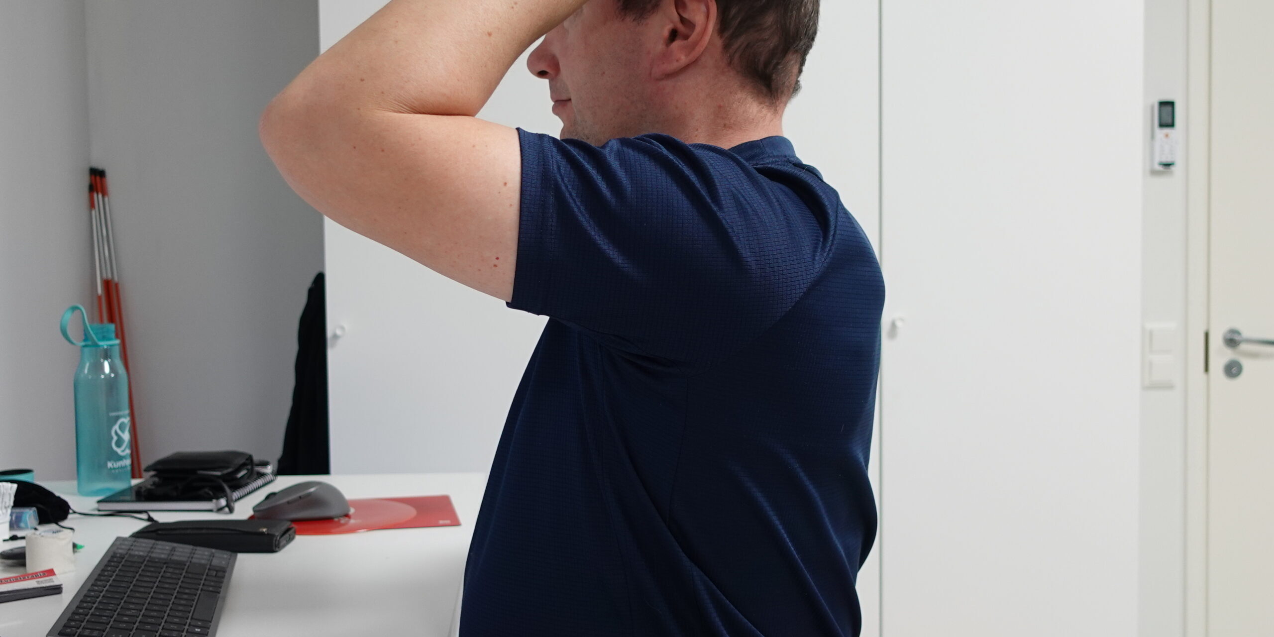 Henkilö istuu näyttöpäätteen äärellä ja pitää päätään korvan yläpuolelta ja takaraivolta, havainnollistaen niska-hartiaseudun kuormitukseen liittyvää päänsärkyä.