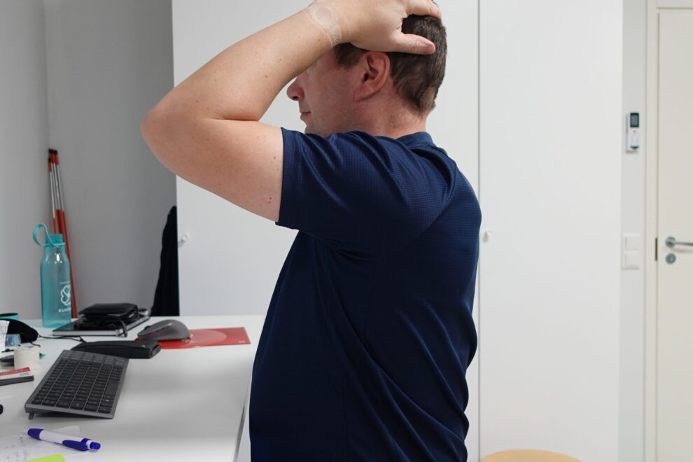 Henkilö istuu näyttöpäätteen äärellä ja pitää päätään korvan yläpuolelta ja takaraivolta, havainnollistaen niska-hartiaseudun kuormitukseen liittyvää päänsärkyä.
